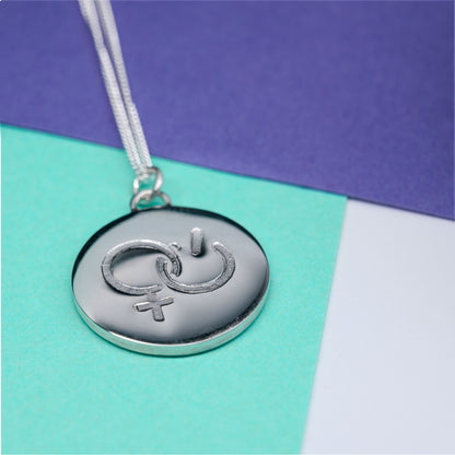 Silver pendant with girl power symbol, on paper