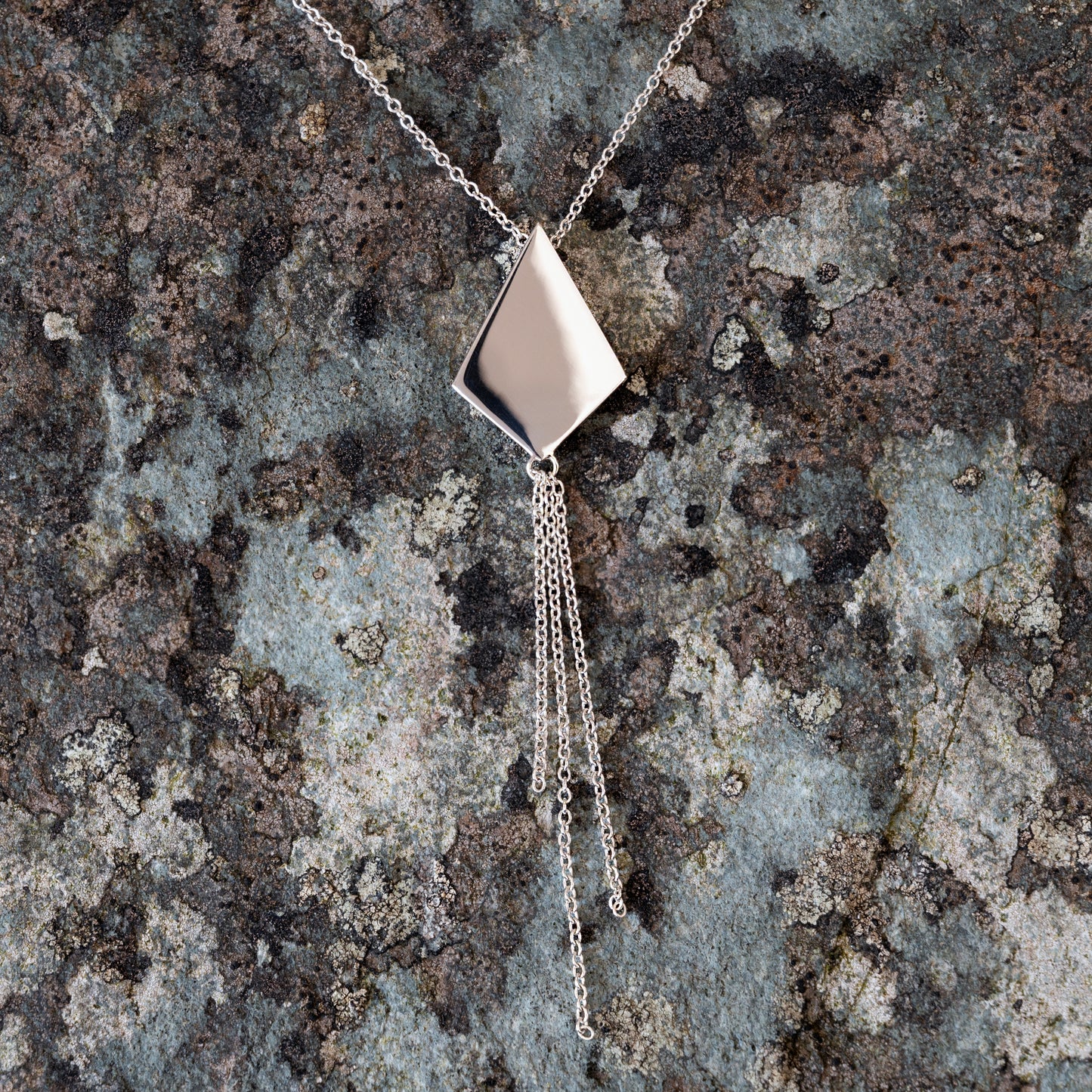 Silver kite shaped necklace with chain tassel on slate background